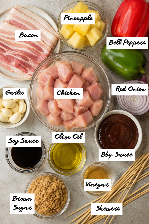 Raw chicken, bacon, pineapple chunks, bell peppers, red onion, and barbecue sauce on a kitchen counter