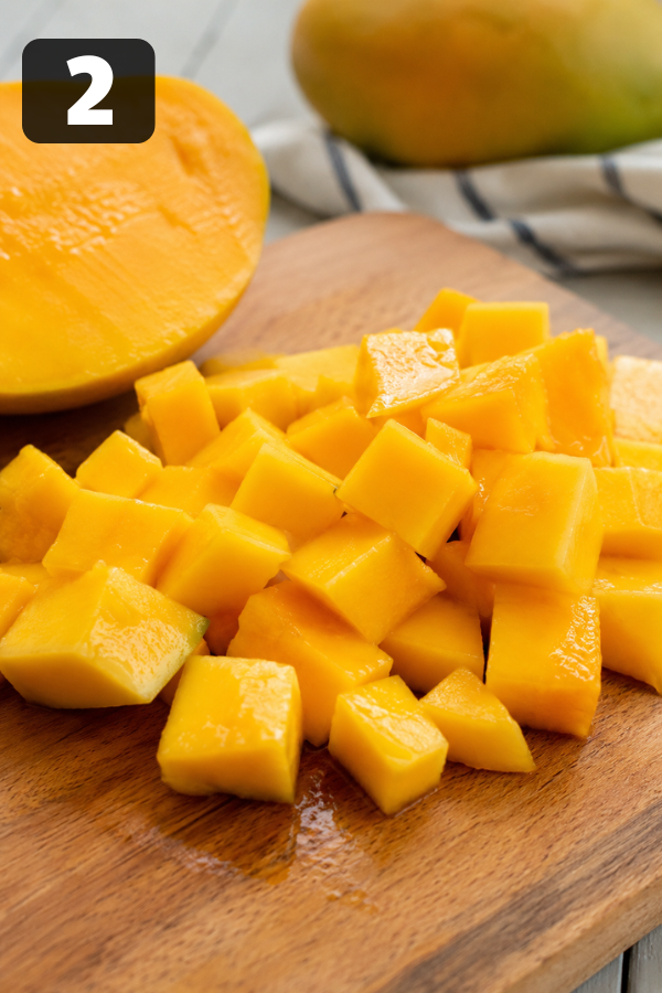Ripe mango being diced into small cubes on a wooden cutting board for a fresh mango avocado salad.