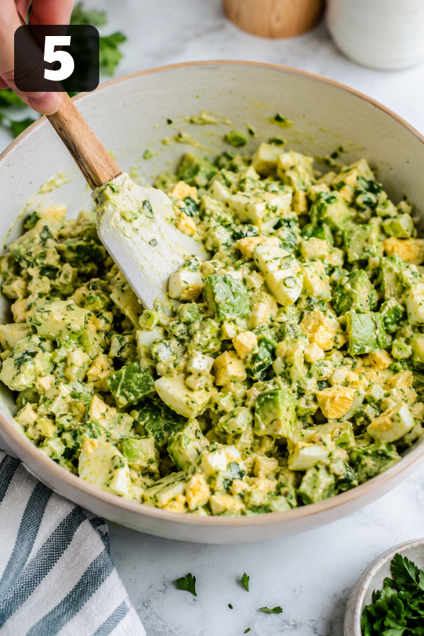 Chopped eggs, avocado, herbs, and dressing gently folded together in a bowl