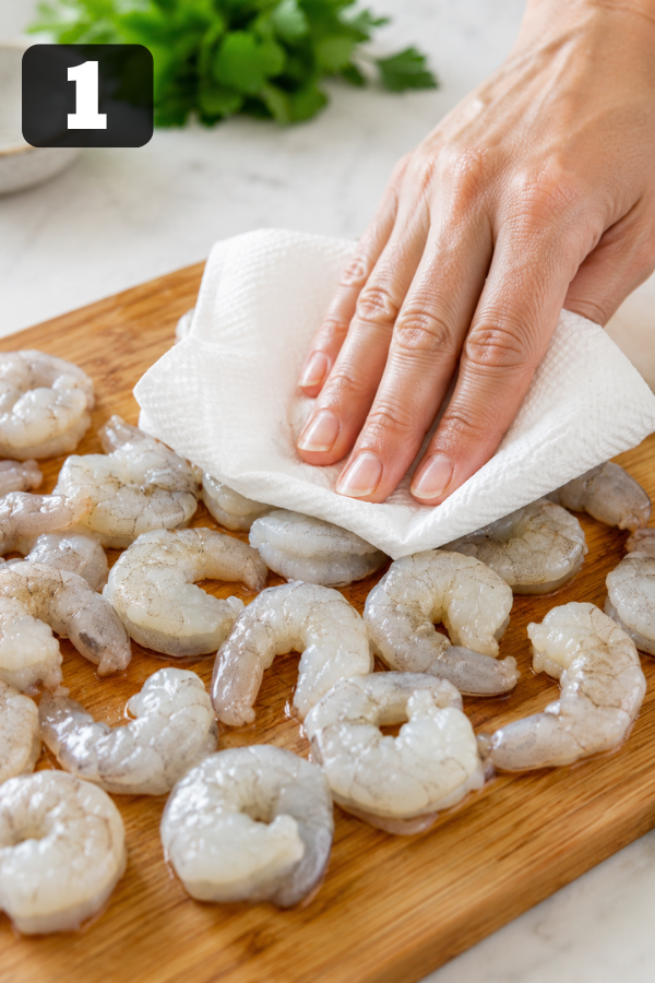 Raw shrimp being thawed, drained, and patted dry with paper towels before seasoning for grilled shrimp bowls.