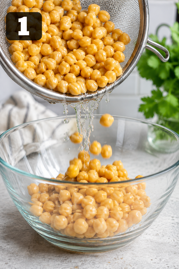 Rinsed chickpeas being added into a large mixing bowl as the base of the salad