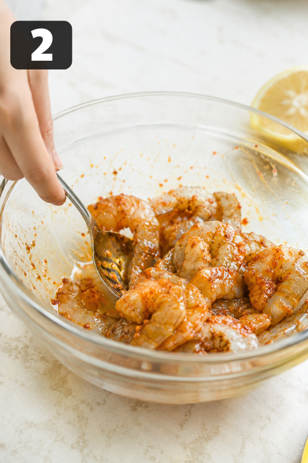 Shrimp tossed with olive oil, chili powder, garlic powder, smoked paprika, cumin, salt, and pepper in a mixing bowl.