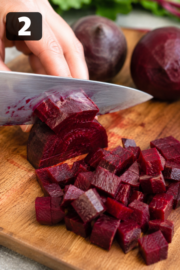 Diced cooked beets added to chickpeas in a bowl, showing vibrant red color mixing