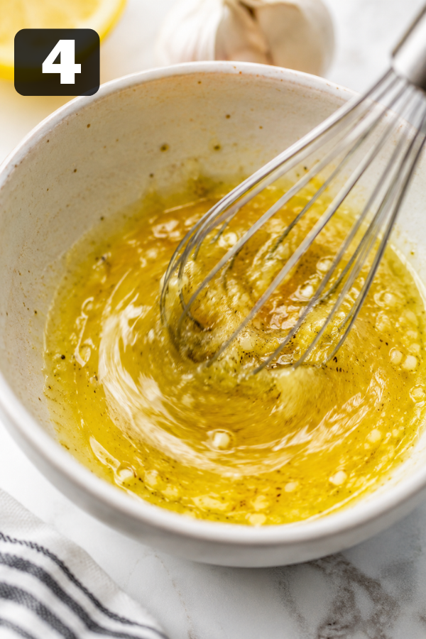 Lemon garlic dressing being whisked in a bowl with olive oil, lemon juice, mustard and garlic
