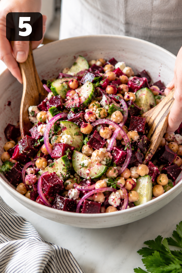 Chickpea beet feta salad being tossed together and topped with crumbled feta cheese and fresh herbs