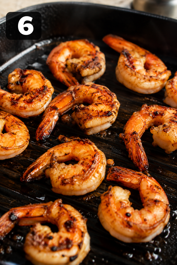 Seasoned shrimp grilling in a hot pan until pink, opaque, and lightly charred on both sides.