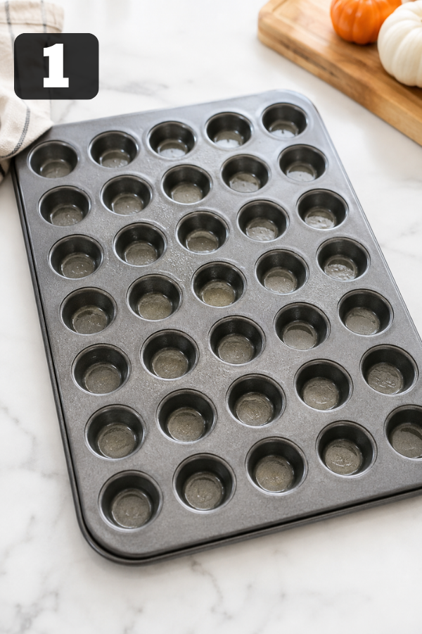 A greased mini muffin pan prepared for baking homemade pumpkin donut holes.
