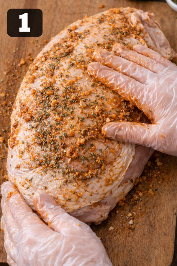 rubbing herb butter seasoning mixture on raw turkey breast on wooden cutting board