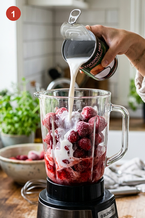pouring coconut milk into blender with frozen strawberries