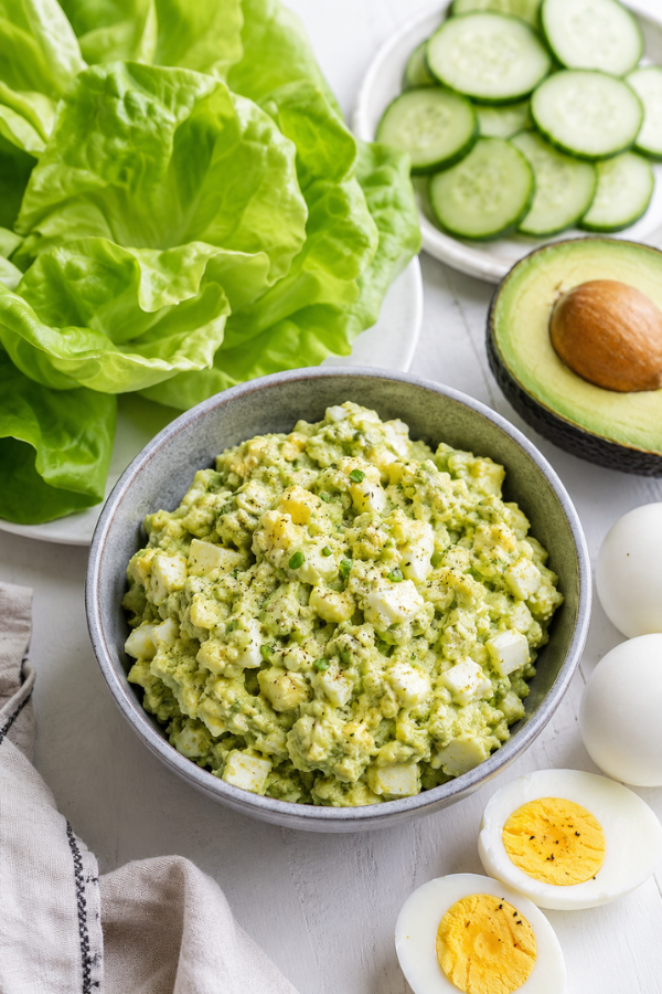 Keto avocado egg salad served in a bowl with chopped eggs, creamy avocado, fresh herbs, and lemon wedges